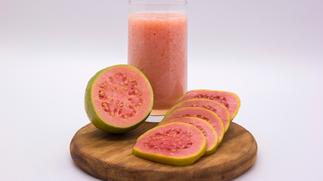 a sliced pink guava fruit on a wooden plate next to a glass of pink juice